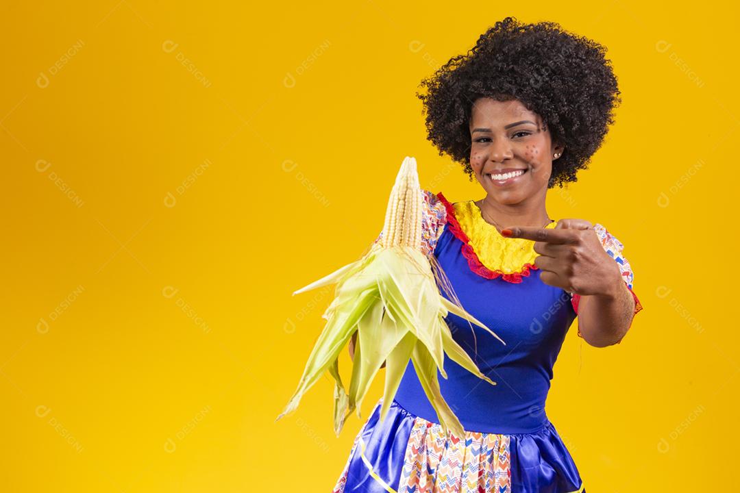 mulher bonita com roupas típicas da festa junina segurando um milho