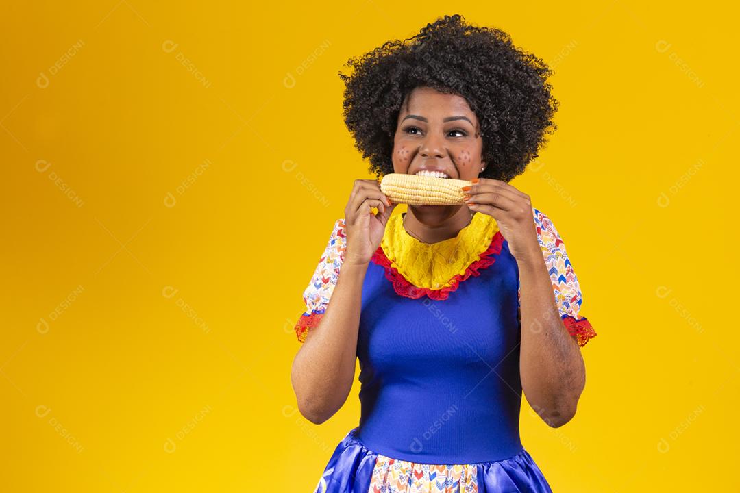 mulher bonita com roupas típicas da festa junina comendo um milho cozido