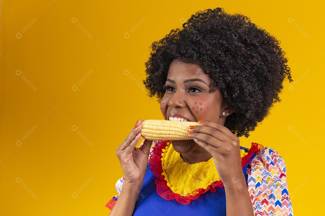 mulher bonita com roupas típicas da festa junina comendo um milho cozido