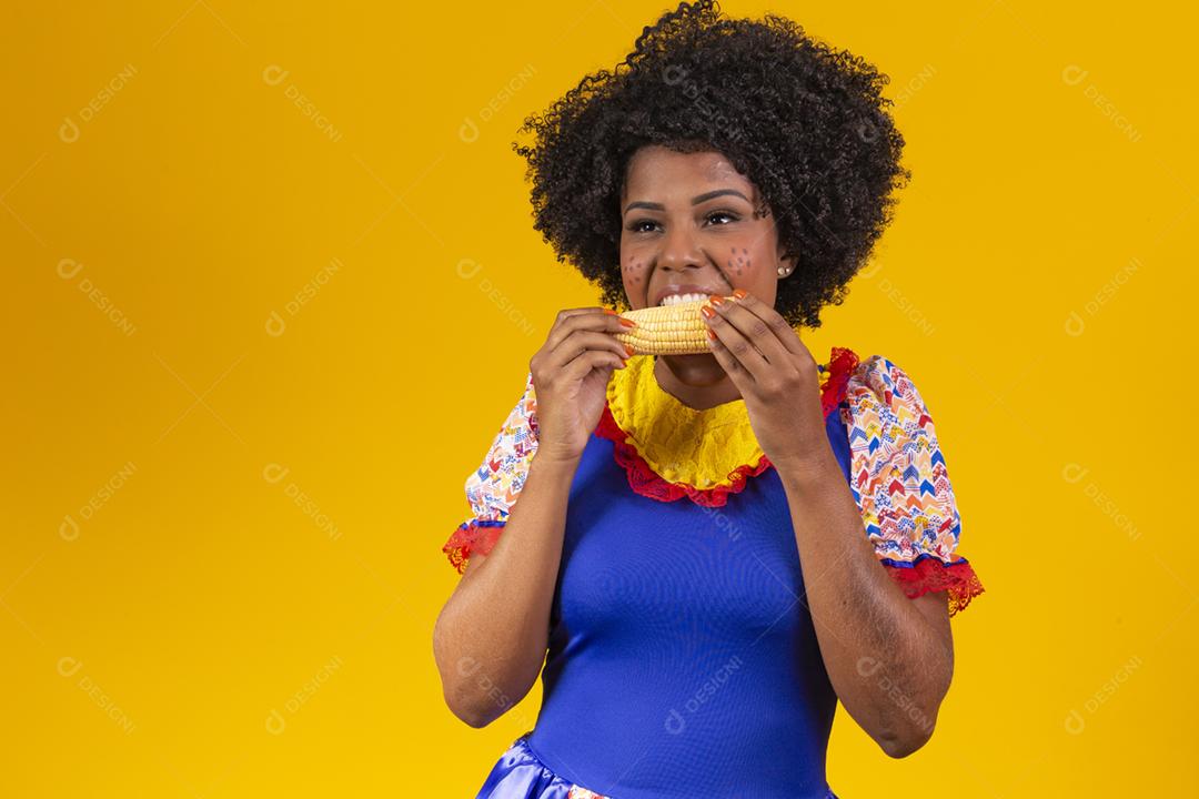 mulher bonita com roupas típicas da festa junina comendo um milho cozido