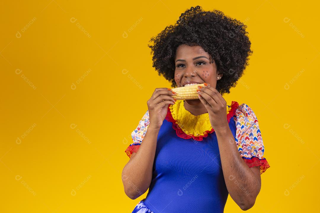 mulher bonita com roupas típicas da festa junina comendo um milho cozido