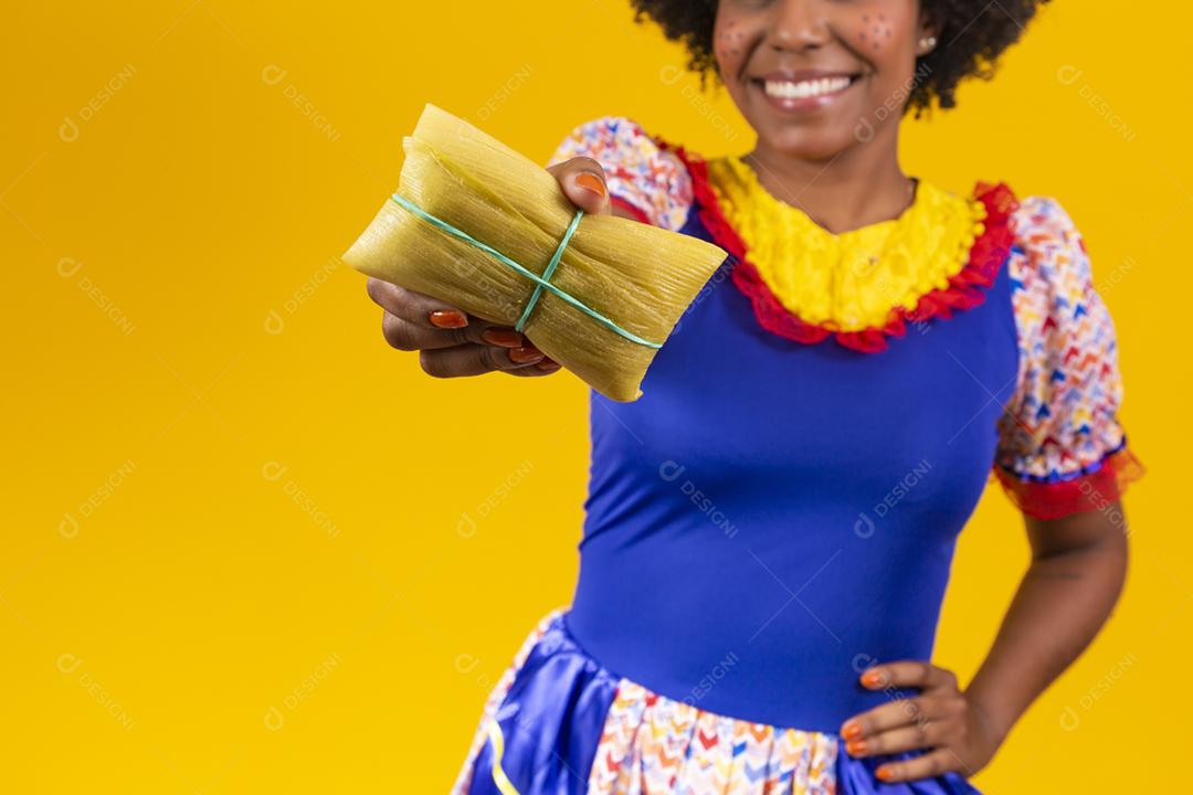 mulher afro em roupas de festa junina segurando um tamale em fundo amarelo