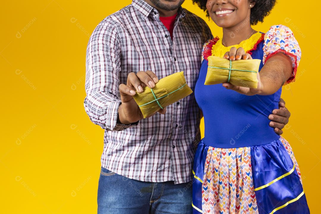 casal de namorados afro em roupas de festa junina segurando uma pamonha