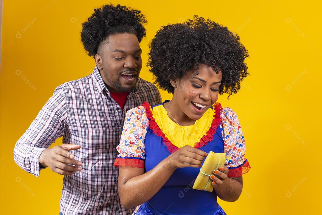 casal de namorados afro em roupas de festa junina segurando uma pamonha