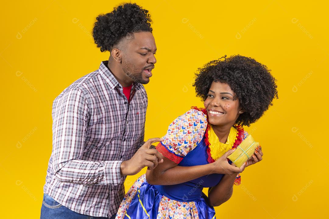 casal de namorados afro em roupas de festa junina segurando uma pamonha