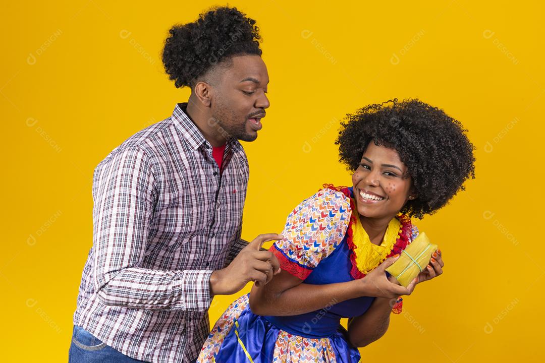 casal de namorados afro em roupas de festa junina segurando uma pamonha