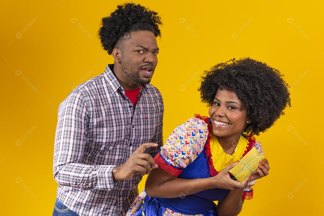 casal de namorados afro em roupas de festa junina segurando uma pamonha