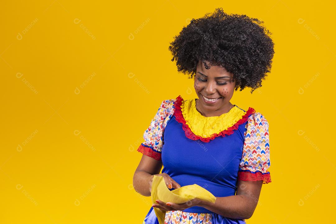 Mulher negra com roupas típicas da festa junina comendo uma deliciosa pam