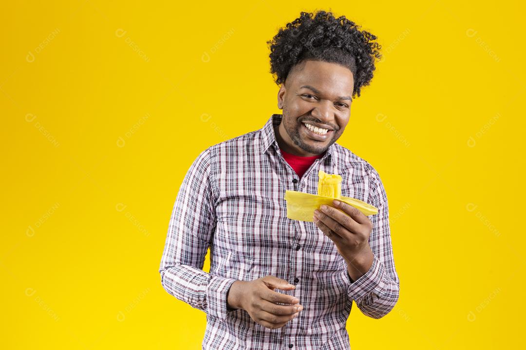Homem negro com roupas típicas da festa junina comendo delicioso pamonha