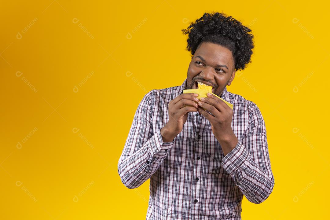 Homem negro com roupas típicas da festa junina comendo delicioso pamonha