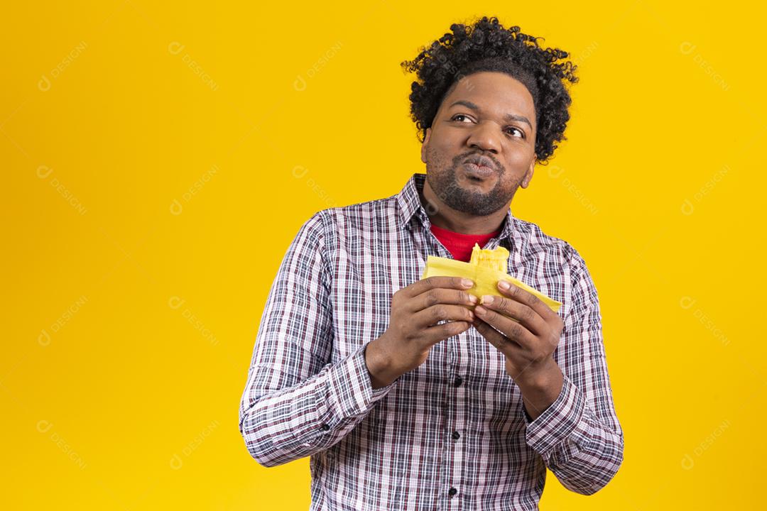 Homem negro com roupas típicas da festa junina comendo delicioso pamonha