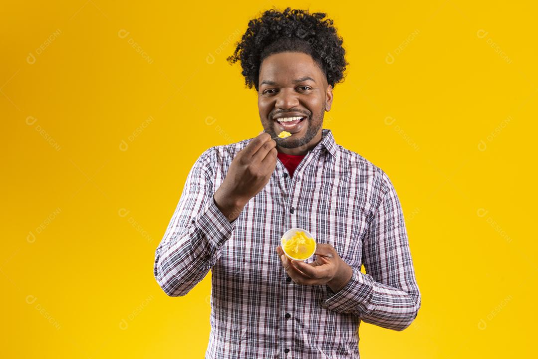 Homem negro com roupas típicas da festa junina comendo delicioso cural
