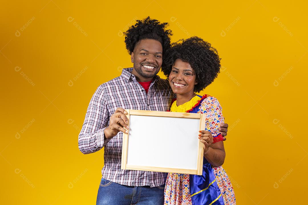 Casal Afro com cabelo afro e roupa de festa junina segurando quadro