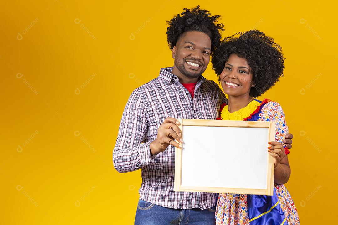 Casal Afro com cabelo afro e roupa de festa junina segurando quadro