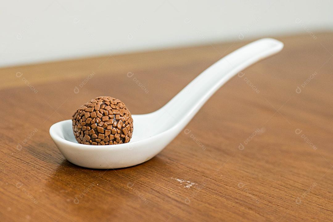 Colher branca com brigadeiro acima de mesa de madeira