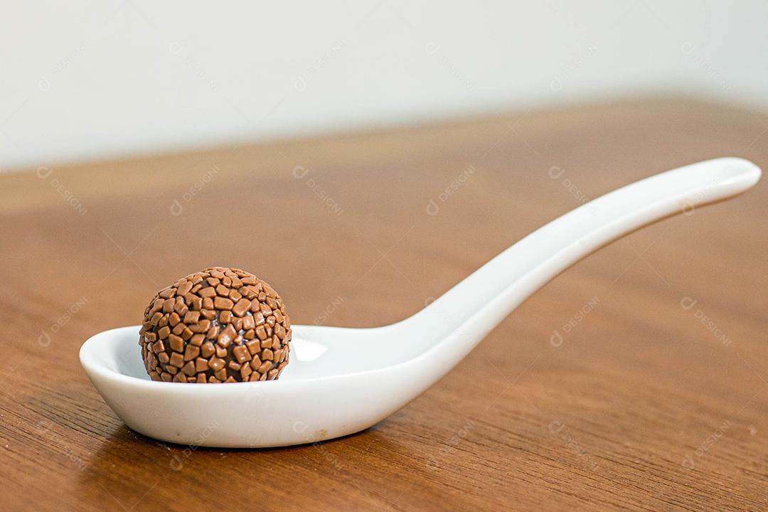 Colher branca com brigadeiro acima de mesa de madeira