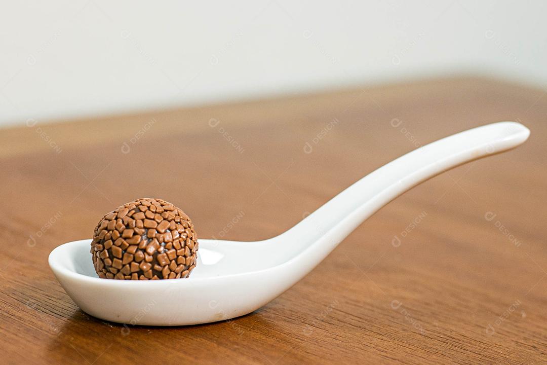 Colher branca com brigadeiro acima de mesa de madeira