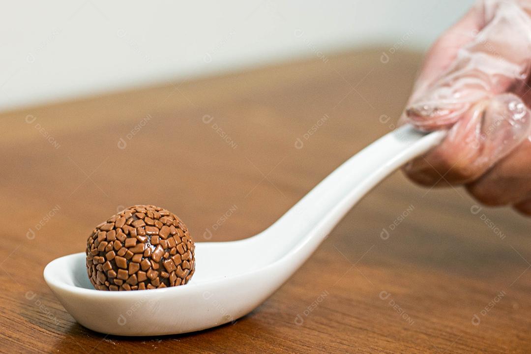 Colher branca com brigadeiro acima de mesa de madeira