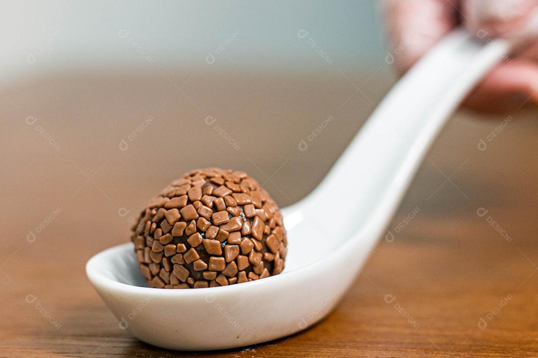 Colher branca com brigadeiro acima de mesa de madeira