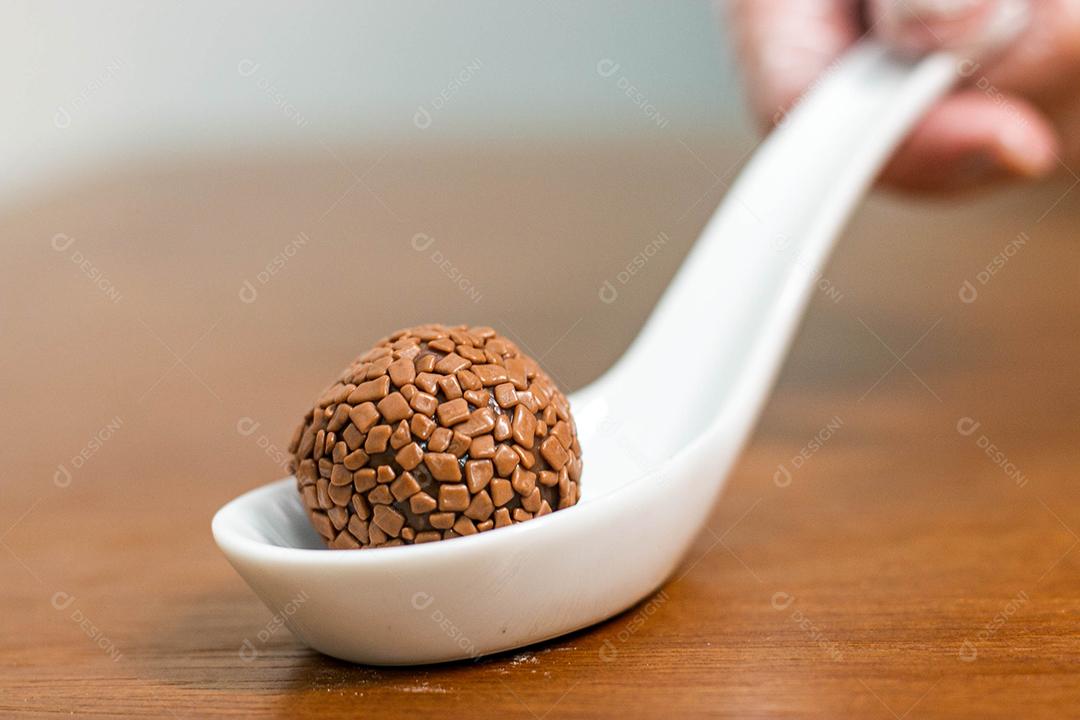 Colher branca com brigadeiro acima de mesa de madeira