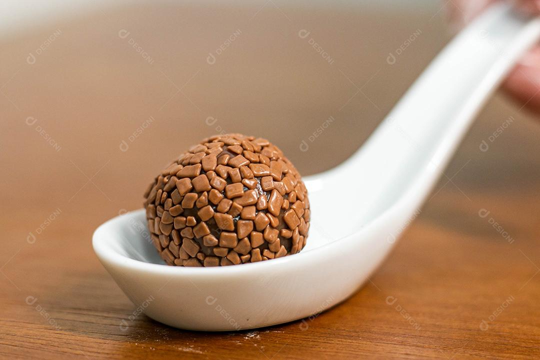 Colher branca com brigadeiro acima de mesa de madeira