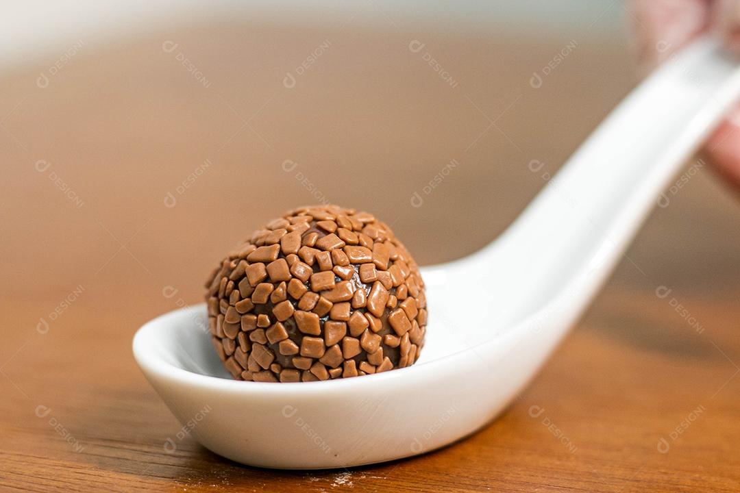 Colher branca com brigadeiro acima de mesa de madeira