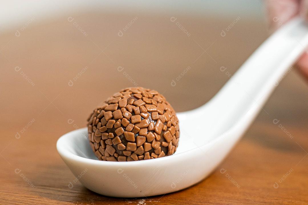 Colher branca com brigadeiro acima de mesa de madeira