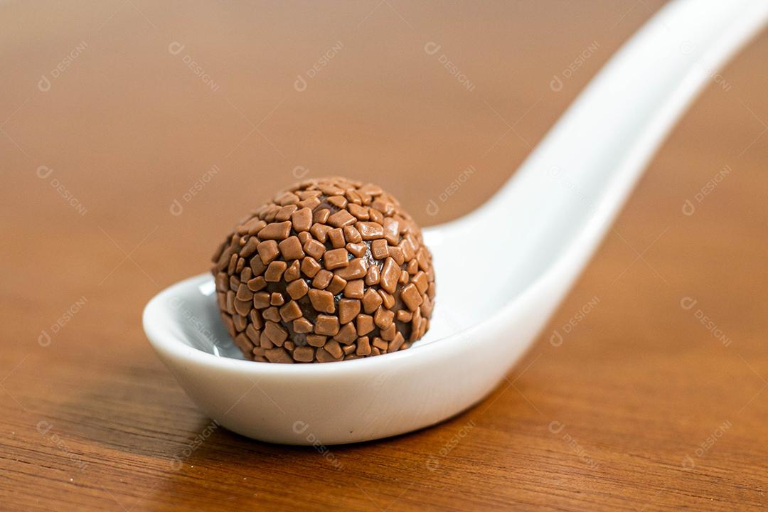 Colher branca com brigadeiro acima de mesa de madeira