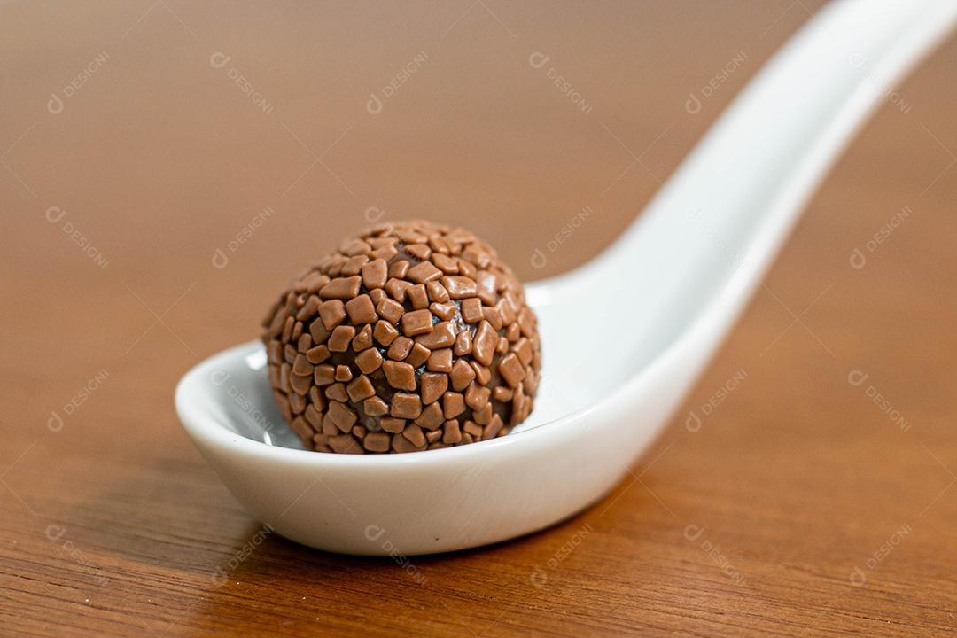 Colher branca com brigadeiro acima de mesa de madeira