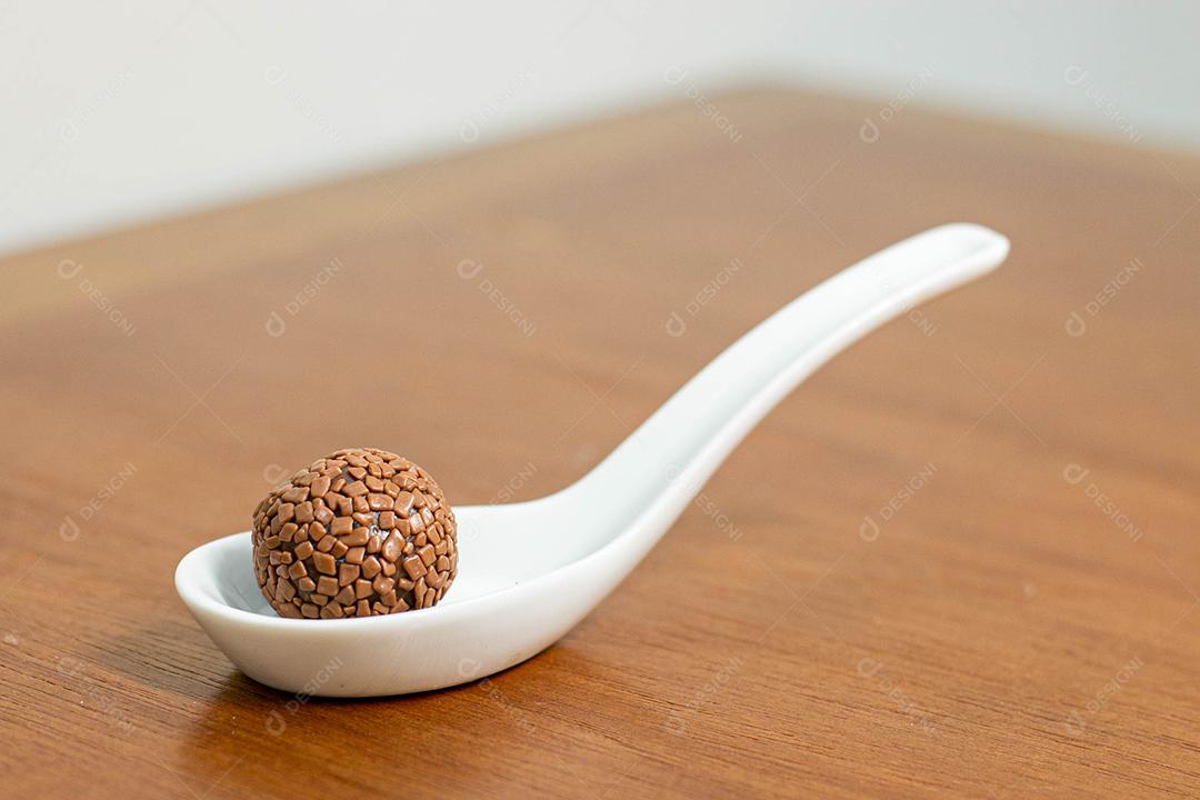Colher branca com brigadeiro acima de mesa de madeira
