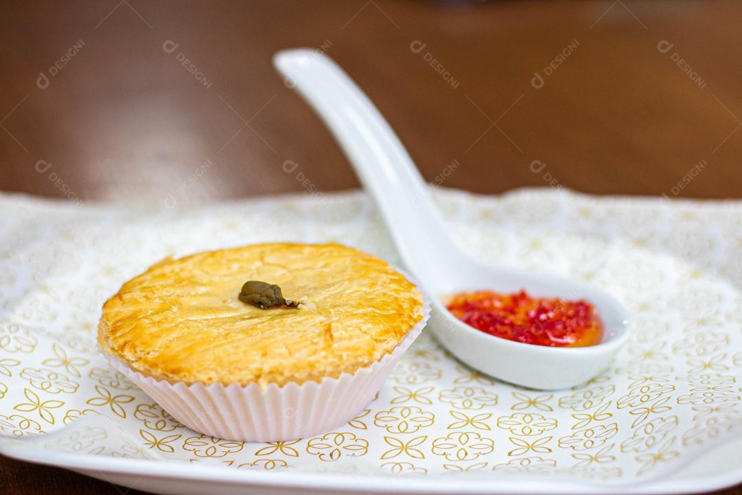 Empadinha em prato branco com colher de temperos acima de mesa