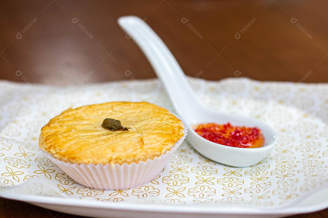 Empadinha em prato branco com colher de temperos acima de mesa