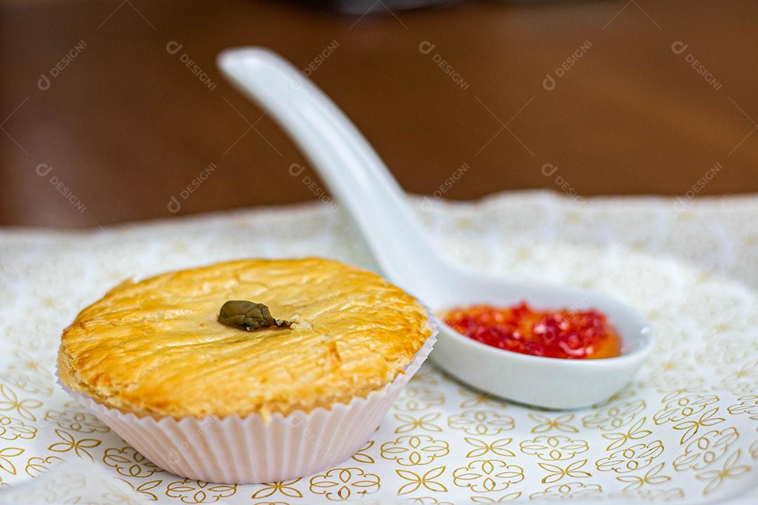 Empadinha em prato branco com colher de temperos acima de mesa