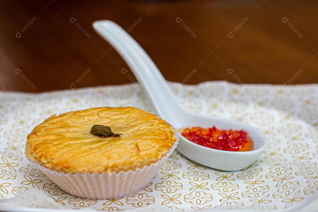 Empadinha em prato branco com colher de temperos acima de mesa