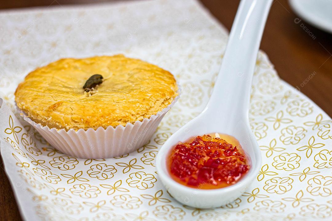 Empadinha em prato branco com colher de temperos acima de mesa