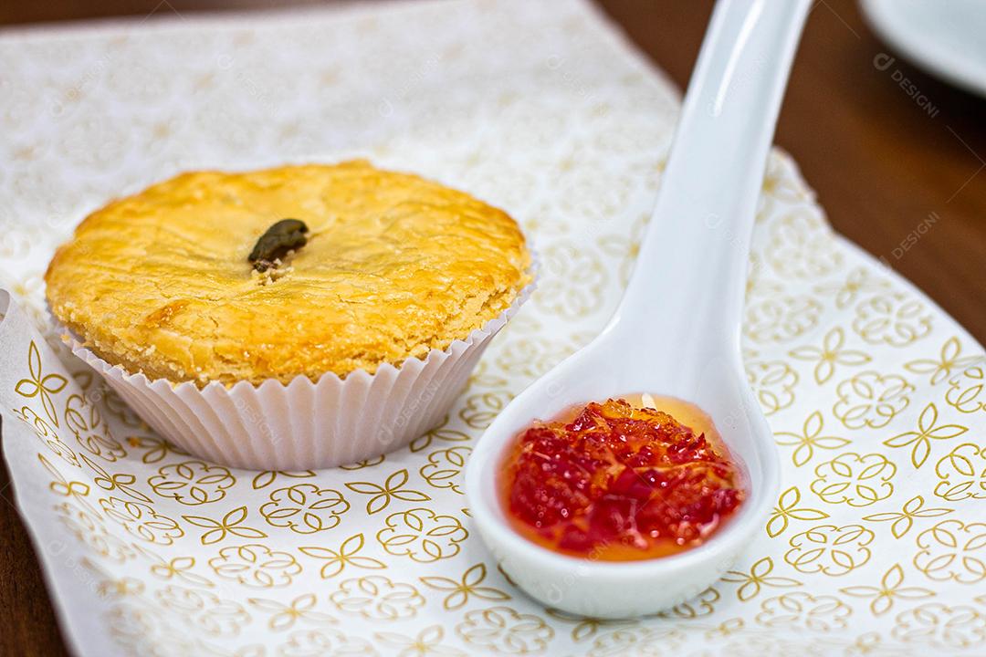 Empadinha em prato branco com colher de temperos acima de mesa