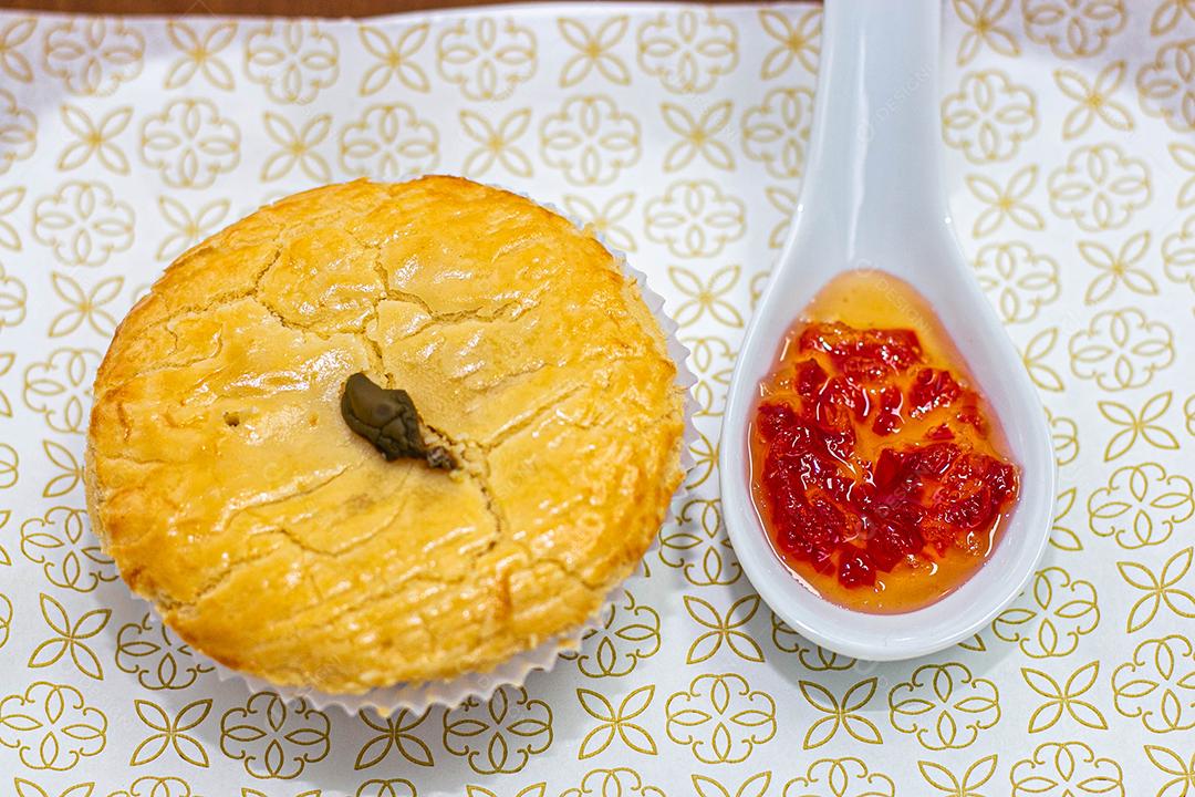 Empadinha em prato branco com colher de temperos acima de mesa