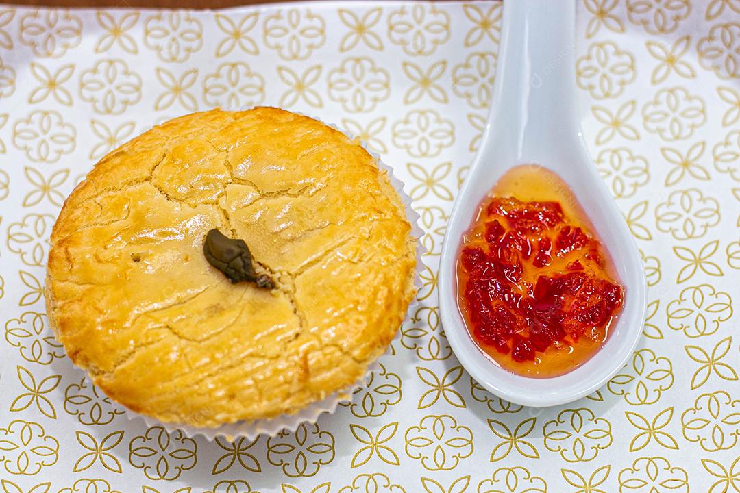 Empadinha em prato branco com colher de temperos acima de mesa