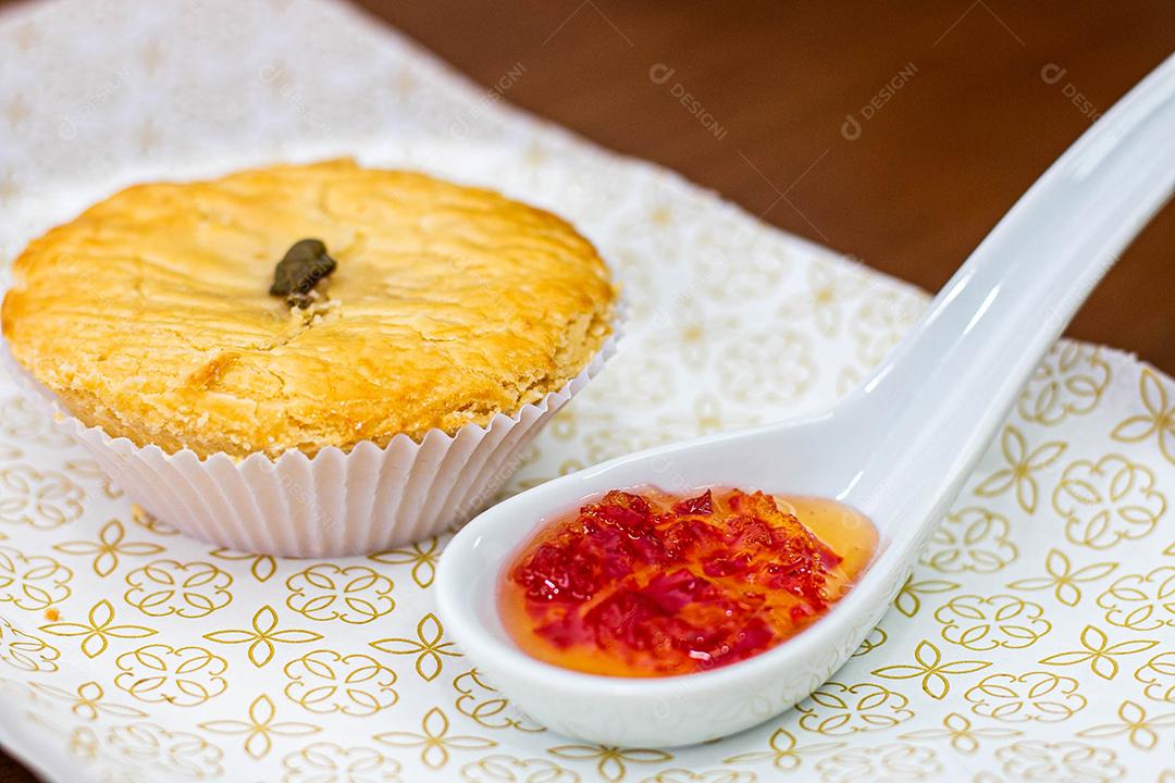 Empadinha em prato branco com colher de temperos acima de mesa