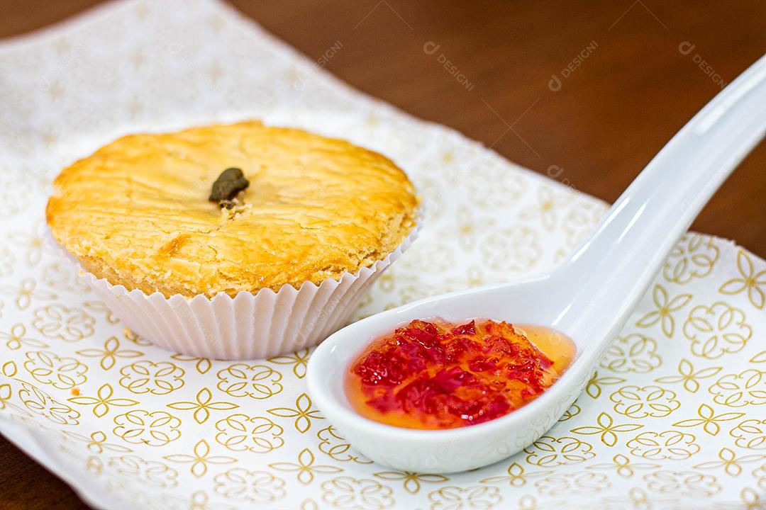 Empadinha em prato branco com colher de temperos acima de mesa