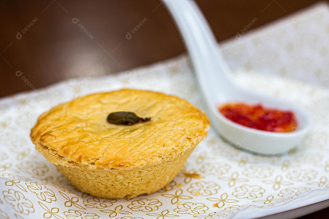 Empadinha em prato branco com colher de temperos acima de mesa