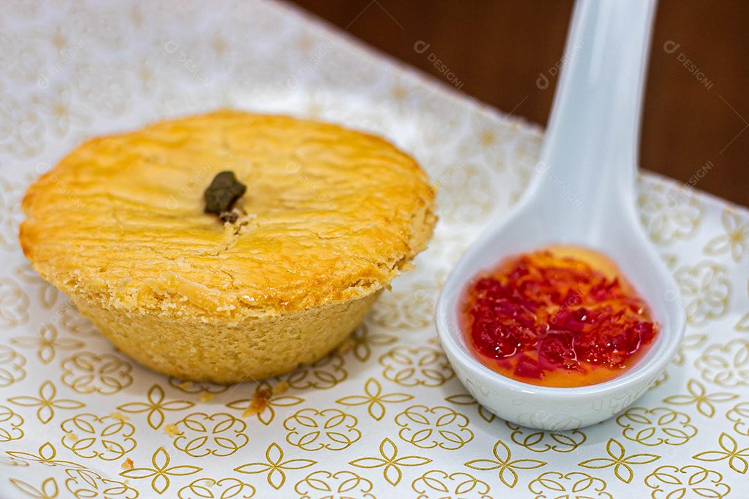 Empadinha em prato branco com colher de temperos acima de mesa