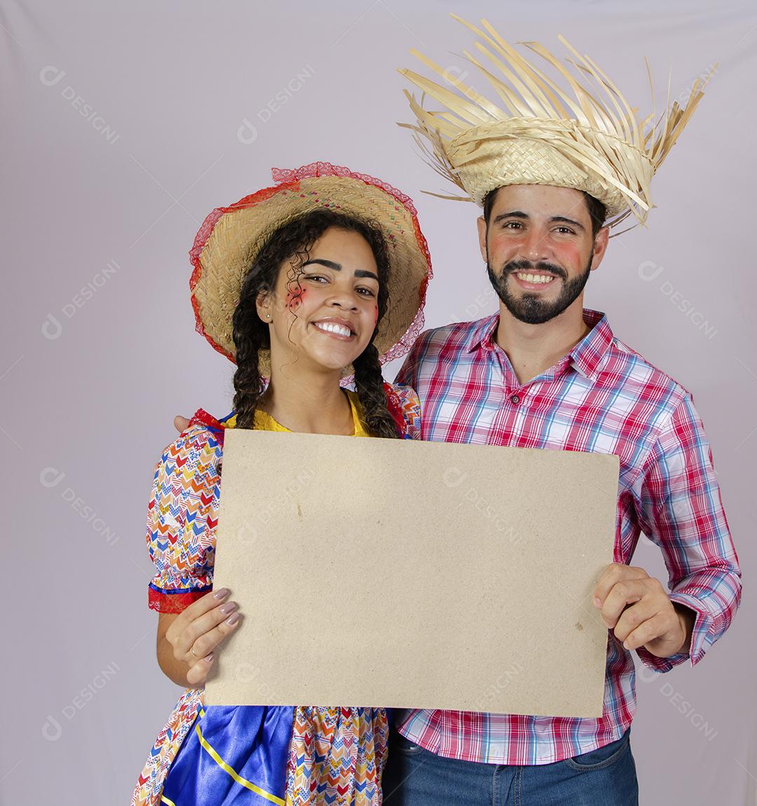 Casal brasileiro vestindo roupas tradicionais para Festa Junina e segurando quadro