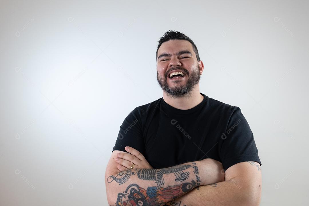 Homem moreno de braços cruzados com camisa preta sorrindo em um branco bac