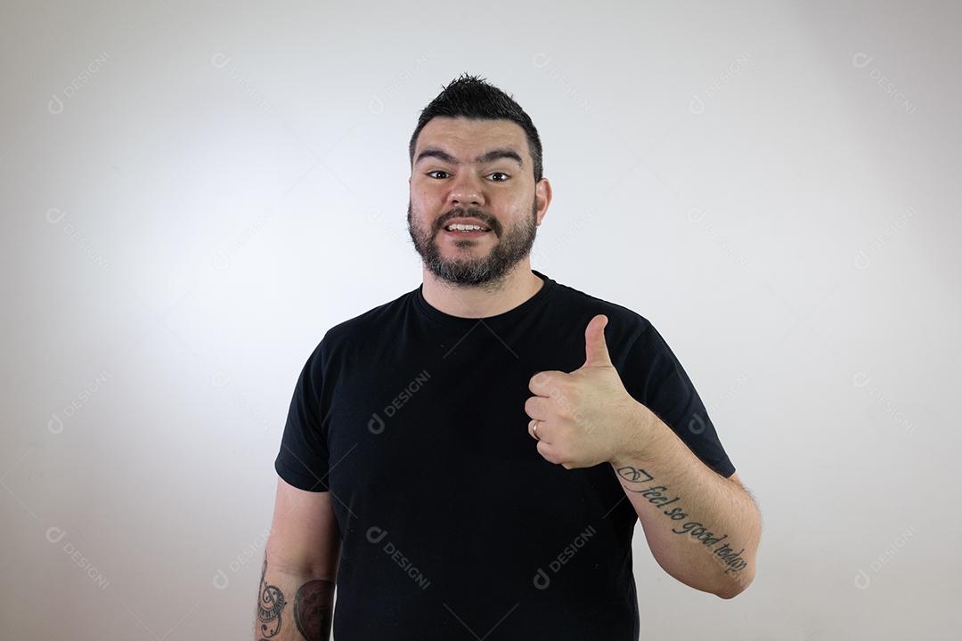 Homem moreno em uma camisa preta, fazendo os polegares para cima em um fundo branco