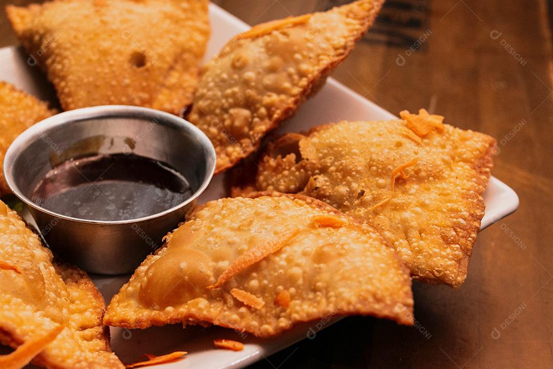 Porção de pastel com salada e molho em cima de mesa
