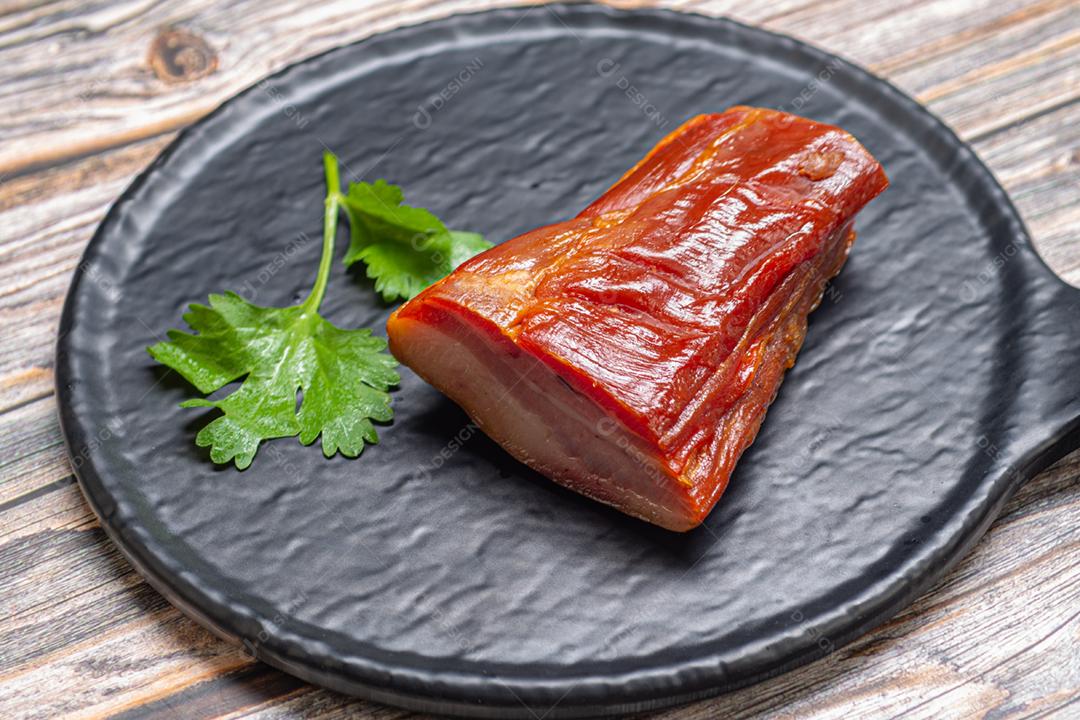 Pedaço de bacon cru servido em um prato sobre uma mesa de madeira