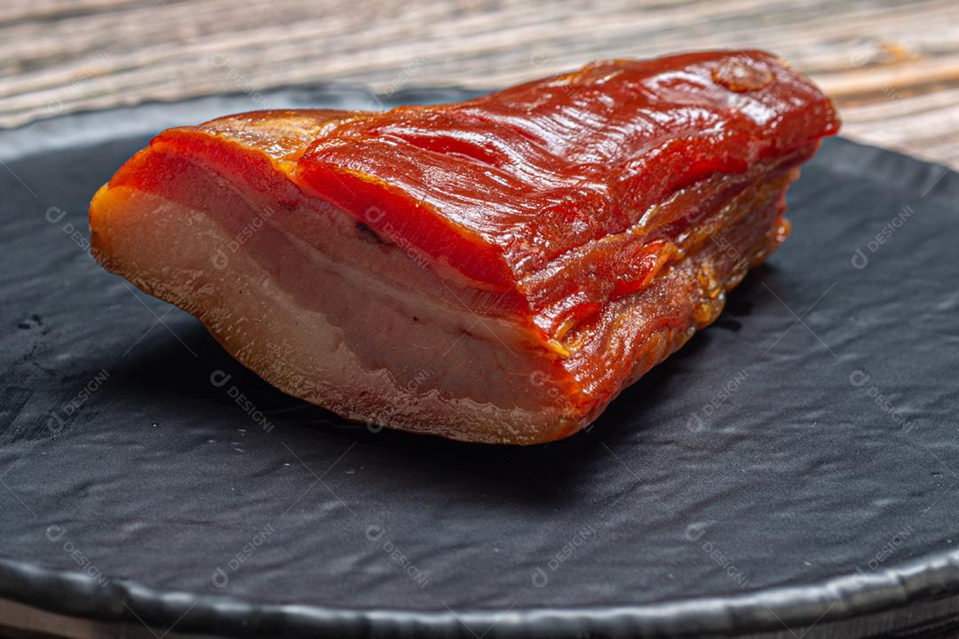 Pedaço de bacon cru servido em um prato sobre uma mesa de madeira