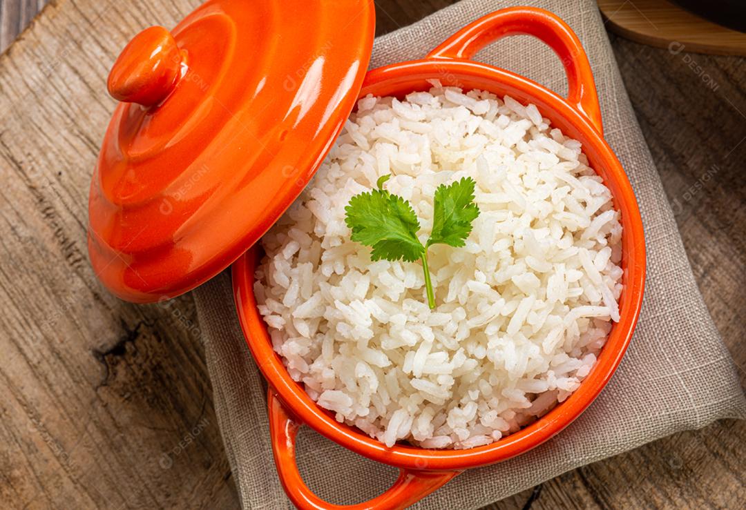 Arroz branco servido em uma tigela de barro em uma mesa de madeira rústica