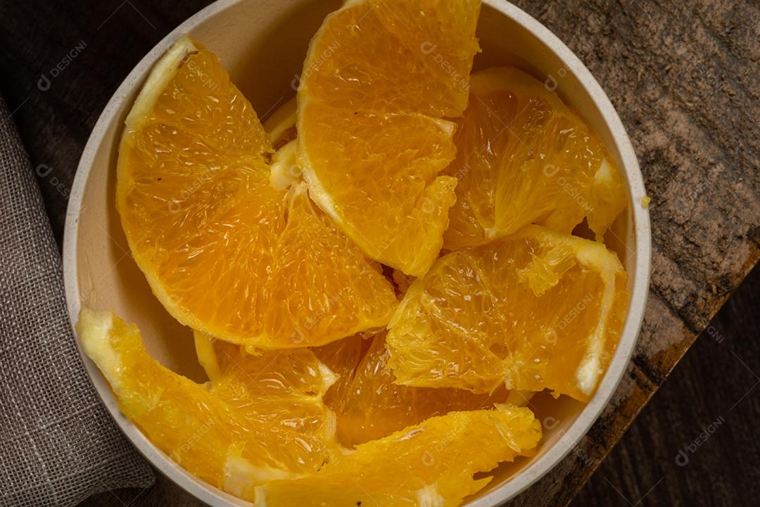 Fatias de laranja servidas em uma tigela de barro na mesa de madeira rústica